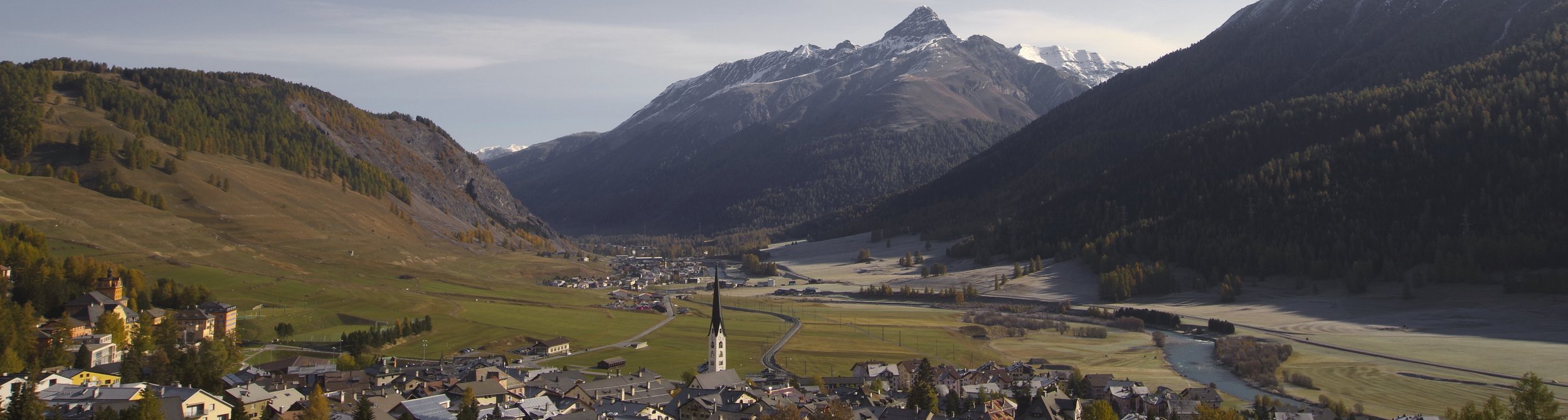 View of a charming chalet nestled against a mountain in Zuoz-Pizzet, Switzerland, showcasing a stunning winter scene. The area is known for skiing, depicted in the distant winter sports activity.