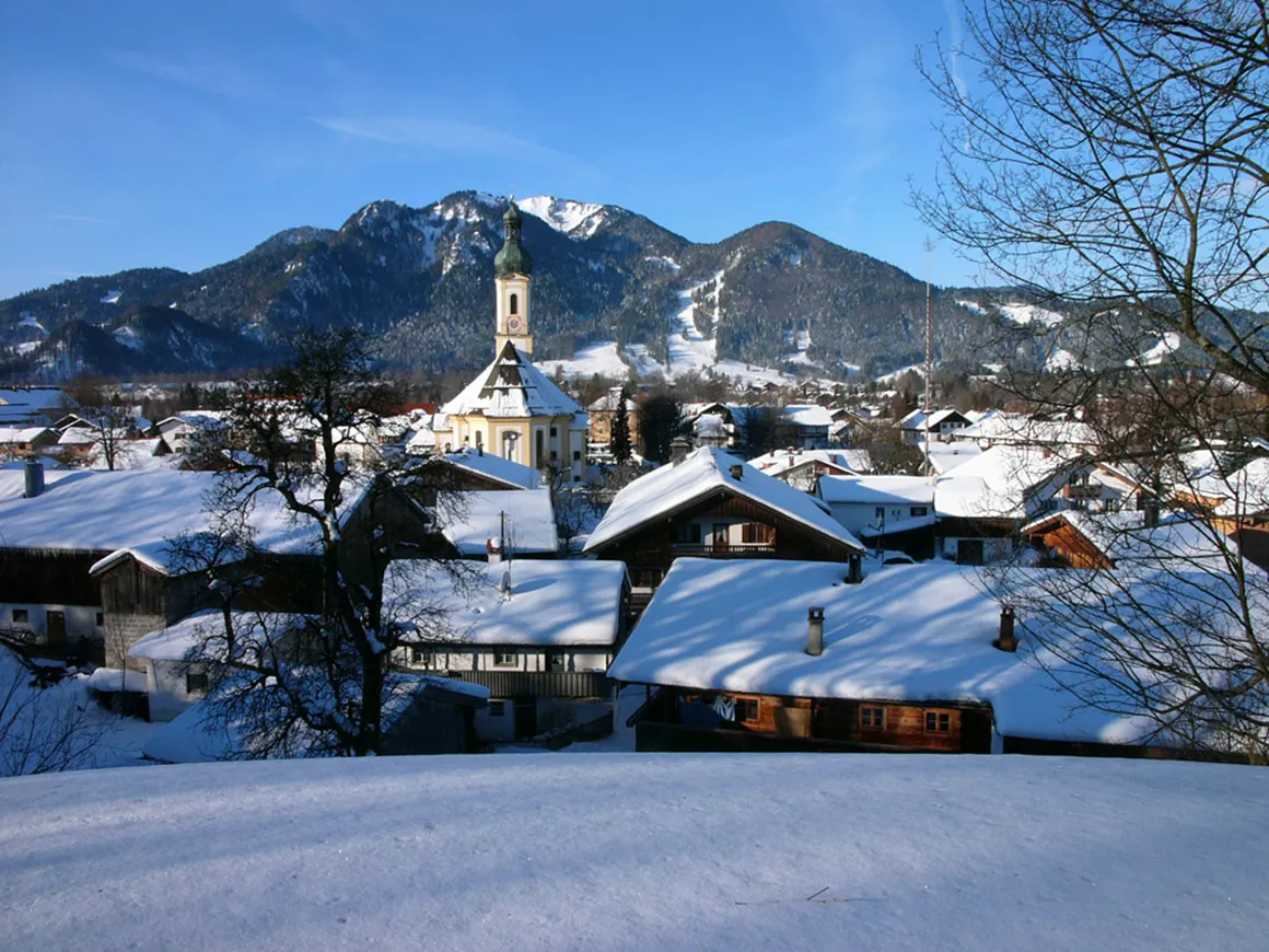 Brauneck – Lenggries | Wegscheid in Germany - a view of a snowy village with mountains in the background.