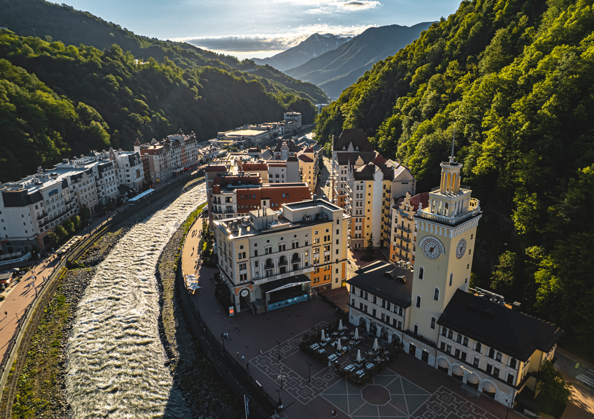 A sunny day at Rosa Khutor, a ski resort in Southern Russia. A chalet can be seen against the backdrop of a mountain, contributing to the wintertime sports atmosphere.