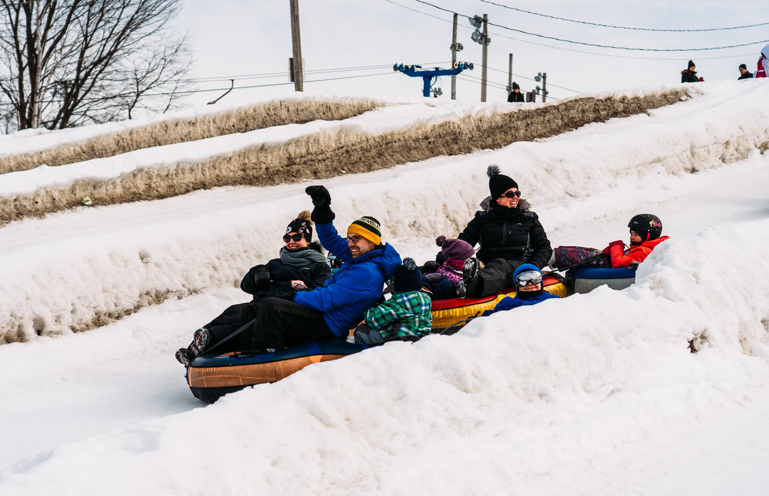 Winter sports scene in Parc de l'Île Melville, Quebec. Snowmobile parked with a ski lift in the background. A family and group of people enjoying skiing in the snowy landscape.