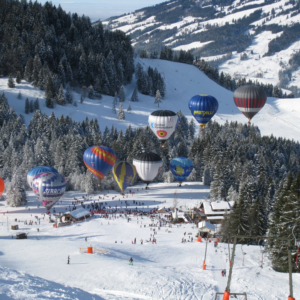 Les Verrières in Switzerland - several hot air balloons are flying over the snow covered mountains.