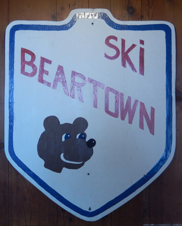 A bustling ski resort in Beartown The Adirondacks New York featuring winter sports enthusiasts. Skiers and a snowboarder can be seen enjoying the crisp white slopes while a ski lift transports others to the top of the mountain.