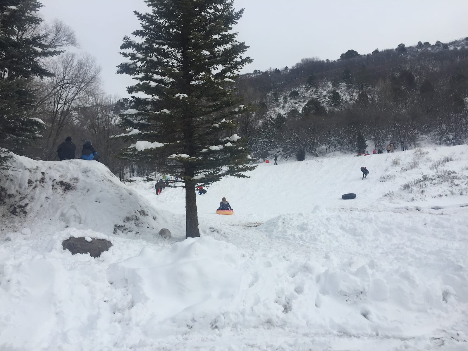A lively winter sports scene at Chapman Hill Durango Colorado showcasing a mountain in the backdrop of a ski resort. Skiers and snowmobiles can be seen enjoying the snow-covered landscape.