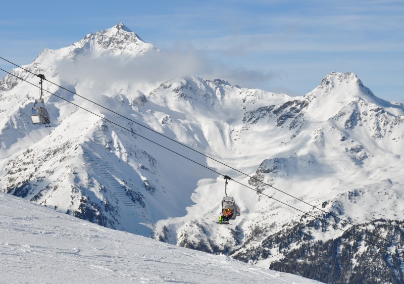 A skier enjoys a snowy day at Bormio – Cima Bianca ski resort in Lombardy Italy. A ski lift ascends the landscape towards a charming chalet contributing to the vivid winter sports scene.
