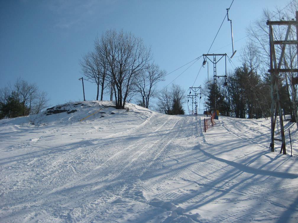 A winter sports scene at Veterans Memorial - Franklin New Hampshire featuring a ski lift in operation surrounded by a ski resort landscape. A skier can be seen enjoying the slopes.