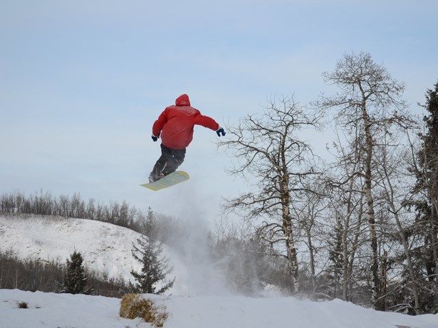 A snowboarder in action at Gwynne Valley Central Alberta Canada demonstrating skill and agility against the breathtaking backdrop of pristine white snow and towering trees.