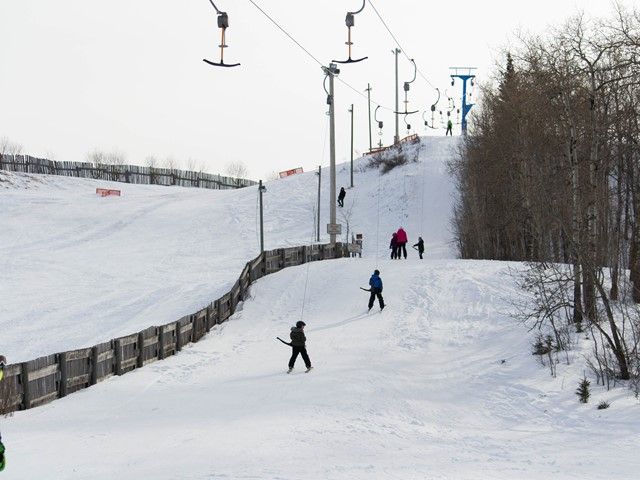 The photo captures the bustling environment of Gwynne Valley ski resort during winter in Alberta Canada with a ski lift visible and a skier in action depicting a typical winter sports scene.