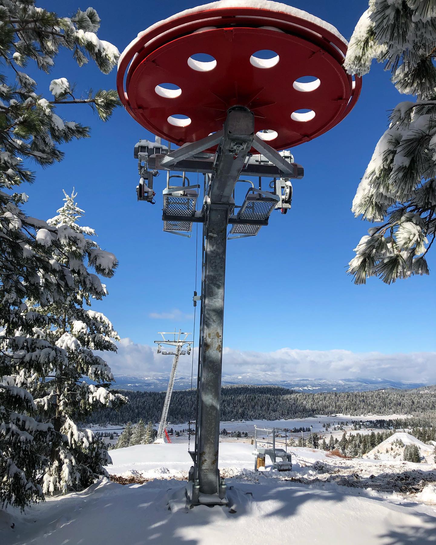 View of Little Ski Hill in Idaho, USA, featuring a ski lift and resort against a wintry landscape. Skiers dot the hill, with a chalet nestled nearby.
