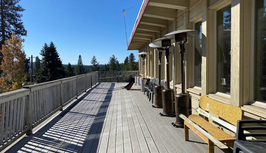 View of a sunny day at Little Ski Hill in Idaho, featuring a lodge, a ski lift, and a chalet which are part of a bustling winter sports center.