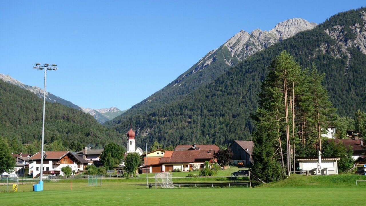 Stanzach in Austria - a green field with houses and mountains in the background.