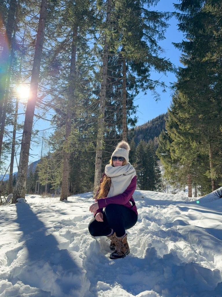 Campo Blenio in Switzerland - a woman kneeling in the snow in front of trees.