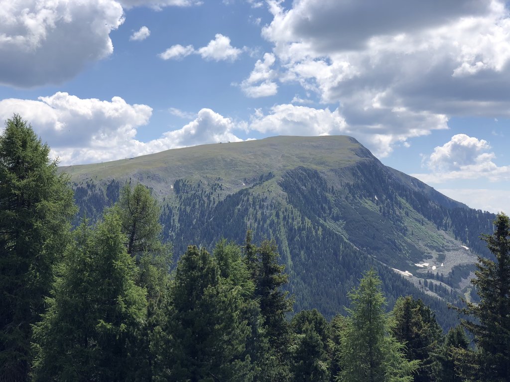 Malga Varena – Passo Lavazè in Italy - a mountain with trees and clouds in the background.