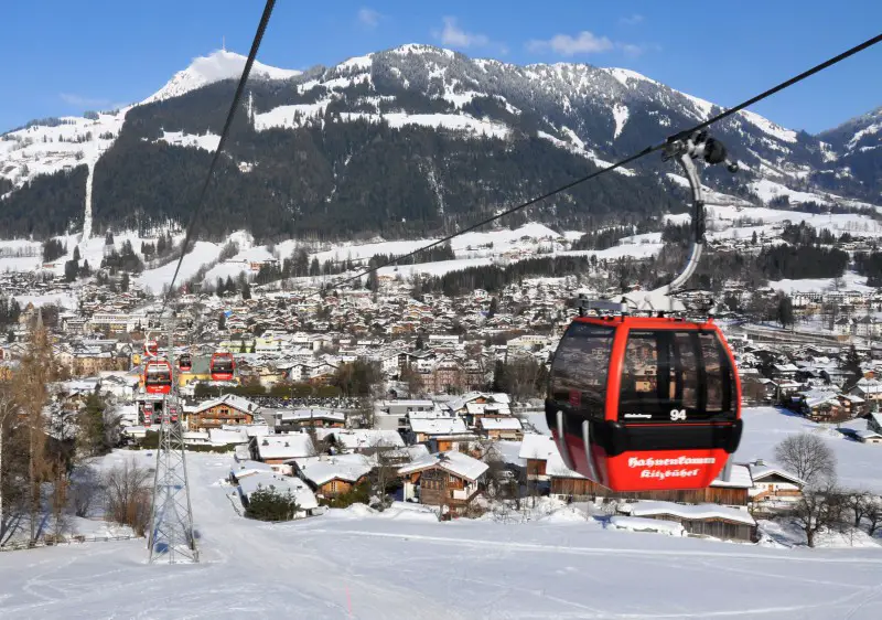 Winter sports scene at Bergbahn AG Kitzbahn - KitzSki in Tyrol, Austria featuring a chalet, ski resort, and ski lift with a skier in action.