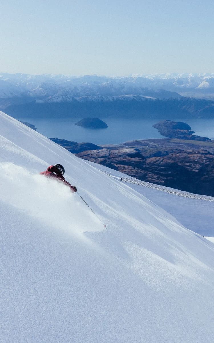 Treble Cone in New Zealand - a person skiing down a snow covered mountain.