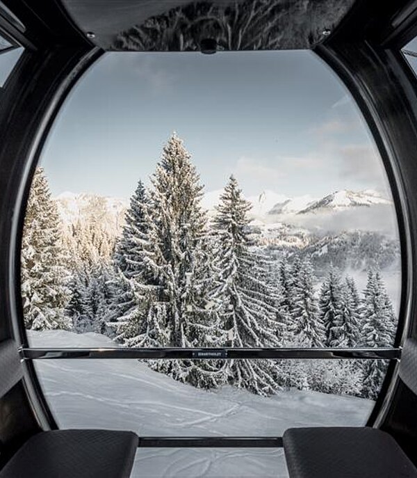A picturesque view of Gstaad in Switzerland displaying a radiant winter scene with a ski lift gracefully making its way through the stunning landscape. A cozy chalet and ski resort add charm to the breathtaking view.