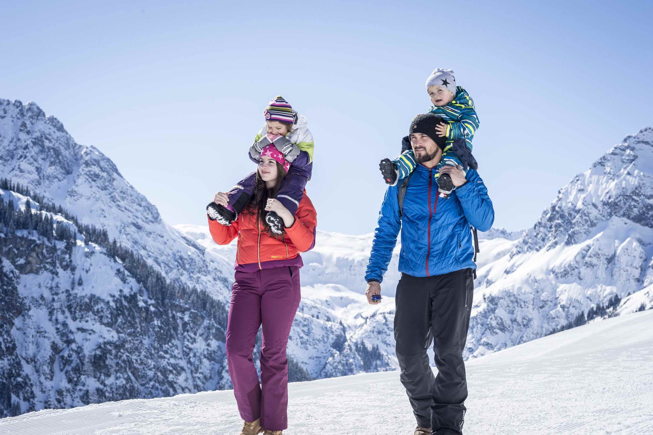 A family enjoying a skiing trip at Walmendingerhorn | ​Heuberg – Mittelberg | ​Hirschegg in Bregenz, Austria, with a quaint challet in the background.
