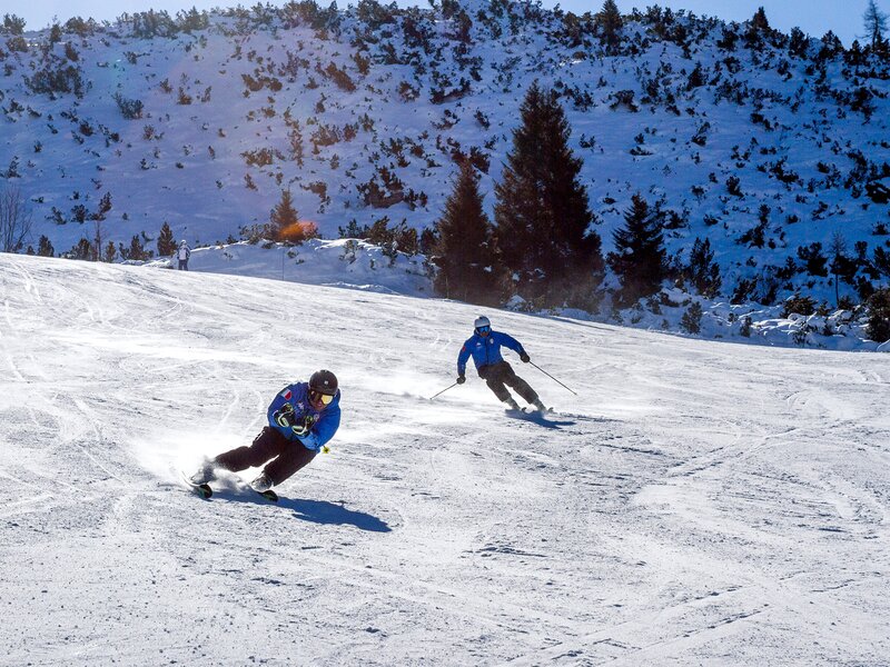 Paganella – Andalo in Italy - two people skiing down a snowy slope in the mountains.