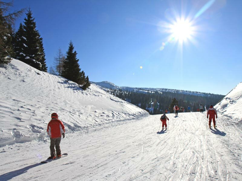 Paganella – Andalo in Italy - a group of people skiing down a snow covered mountain.