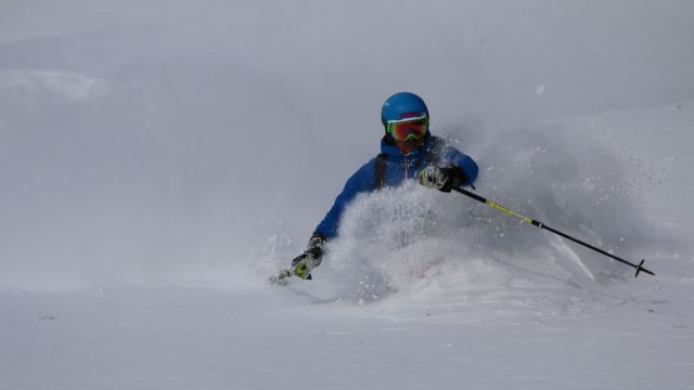 A skier swiftly glides down the snowy slopes at Wurzeralm – Spital am Pyhrn with a charming chalet and ski resort in the background encapsulating a vibrant winter sports scene in Steyr-Kirchdorf Austria.