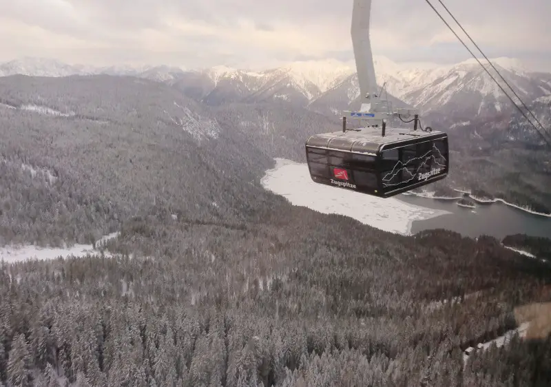 A picturesque view from Zugspitze Upper Bavaria. The main highlight is a ski lift with a bustling ski resort near it. Ski enthusiasts can be seen enjoying their winter sport amidst the stunning mountain scenery.