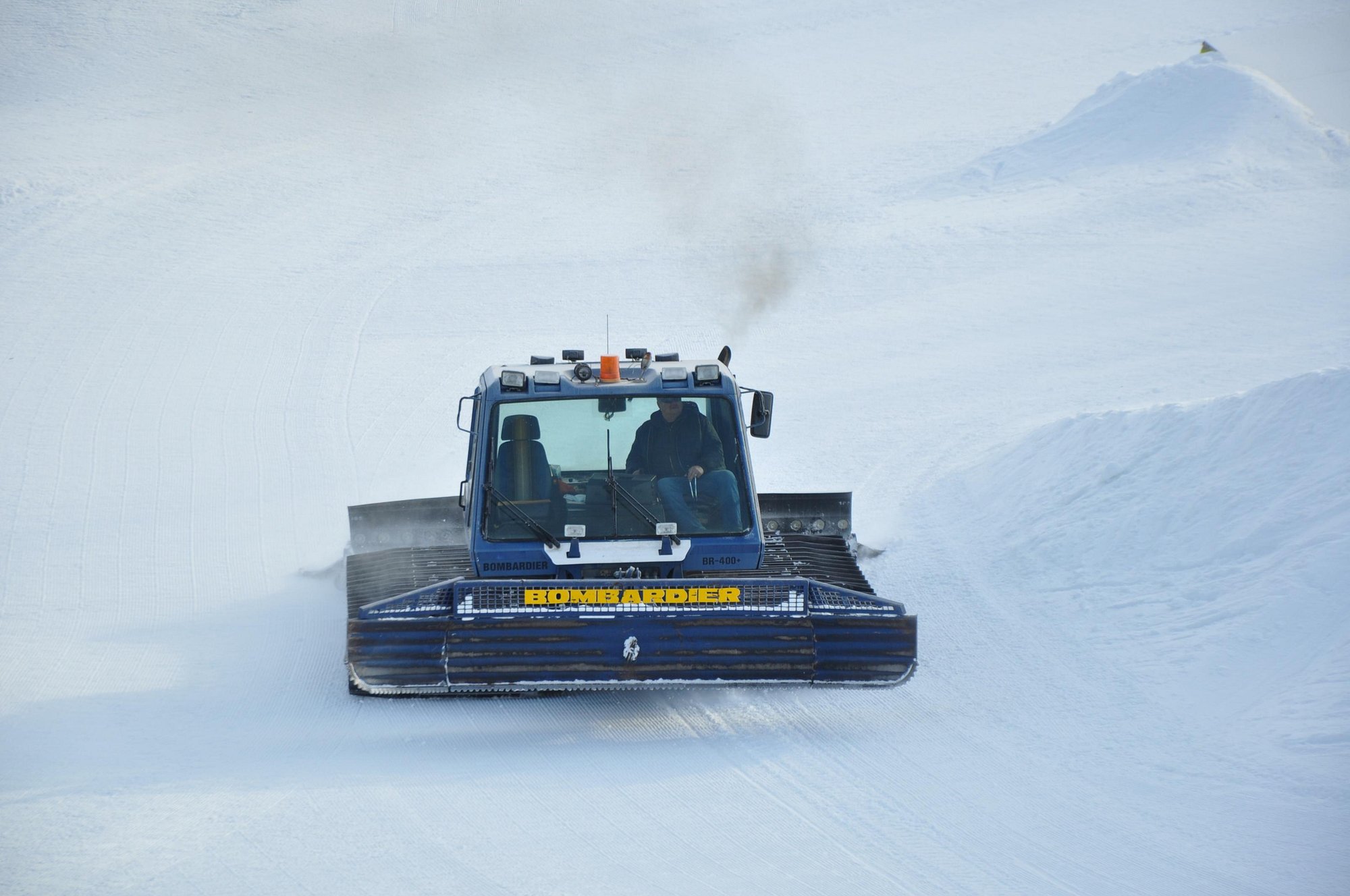 A snowmobile parked at Stony Mountain in Manitoba Canada with a chalet and winter sports centre in the backdrop. A skier and signs of winter sports activities are lightly visible.