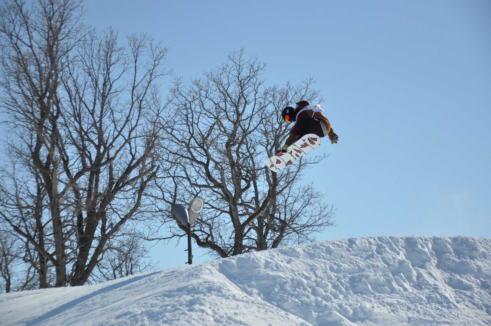 A snowboarder glides down a slope at Stony Mountain, Manitoba, Canada. The winter landscape is blanketed in fresh white snow, portraying the thrill and tranquility of snowboarding.