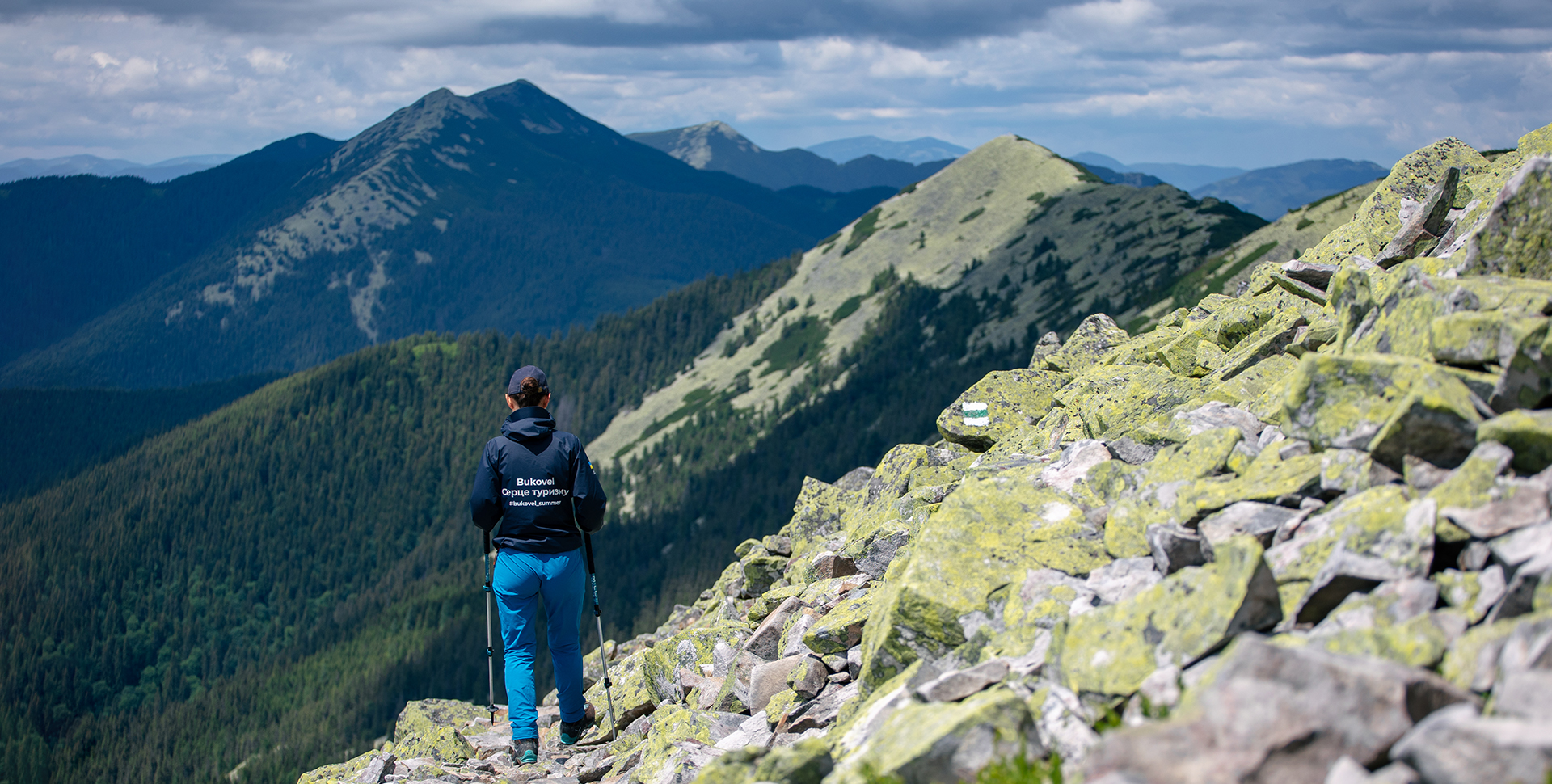 Breathtaking view of Bukovel, Ukraine featuring a towering mountain dusted in snow and a charming chalet nestled at its base. A skier and a parked mountain bike hint at the active lifestyle embraced here.