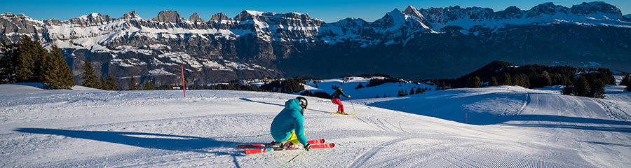 A skier is gliding down the snow-covered slope of Flumserberg ski resort in Heidiland, Eastern Switzerland. A picturesque chalet can be seen nestled amidst the winter setting.