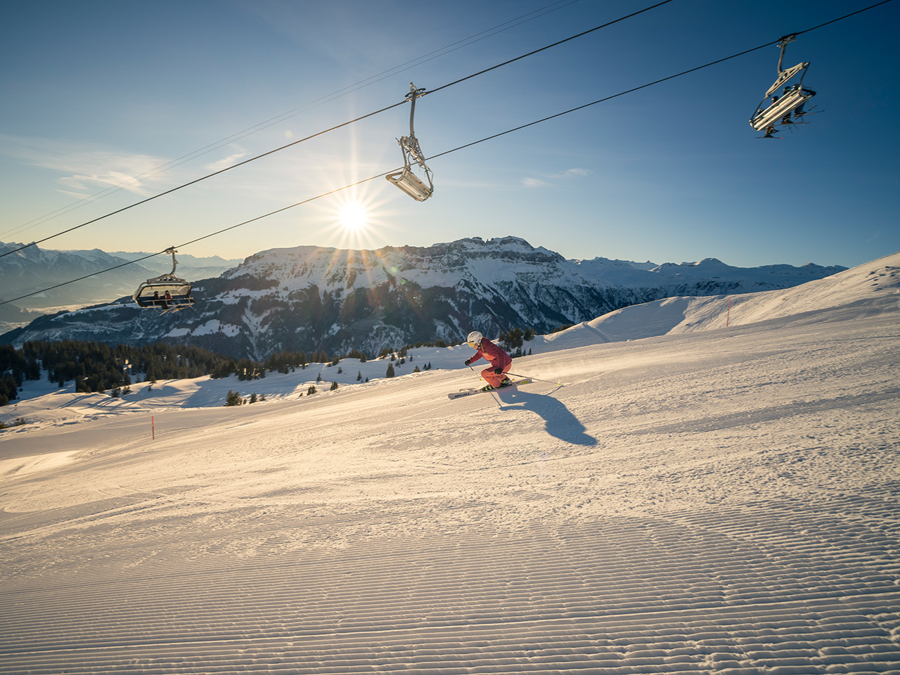 Winter sports scene at Flumserberg in Heidiland, Eastern Switzerland. A skier takes on a snowy slope amidst a picturesque ski resort with a ski lift and cosy chalet in the backdrop.