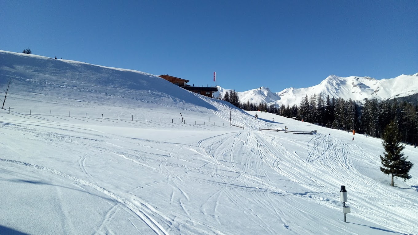 Arena Bergeralm in Austria - a snow covered slope with trees and mountains in the background.