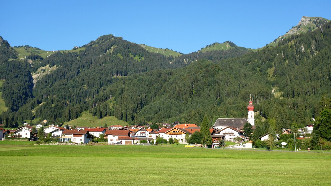 Hahnenkamm – Höfen | ​Reutte in Austria - a green field with houses and mountains in the background.