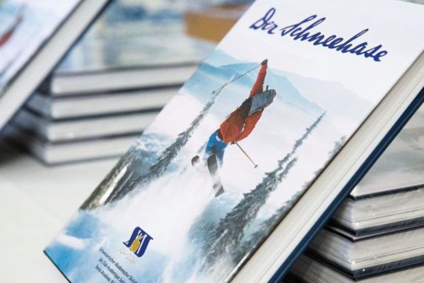 A skier making their way down a snowy slope in Hahnenkamm - Höfen | ​Reutte, Außerfern, Tyrol, Austria. A charming chalet and scenic winter sports scene visible in the backdrop.