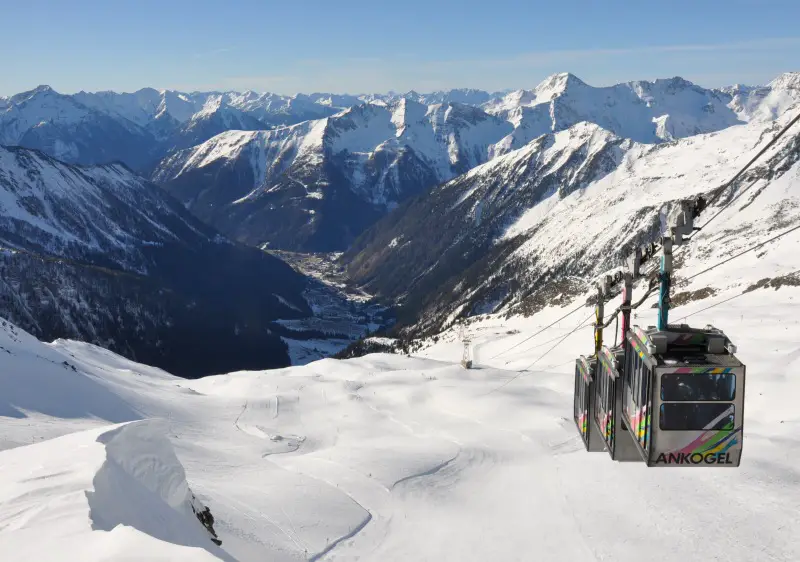 A winter sports scene at Axamer Lizum ski resort in Tyrol, Austria. Features a ski lift and a ski runner, with a chalet in the background.