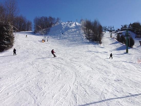 A winter sports scene at Hockley Valley in Southern Ontario. A ski resort boasts a chalet, skiers and a ski lift detailing a busy day on the slopes.