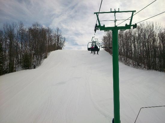 A winter scene at Hockley Valley Ontario featuring a ski lift ascending a snow-covered mountain and a skier descending. A chalet can be seen in the distance encapsulating the bustling activity of a ski resort.