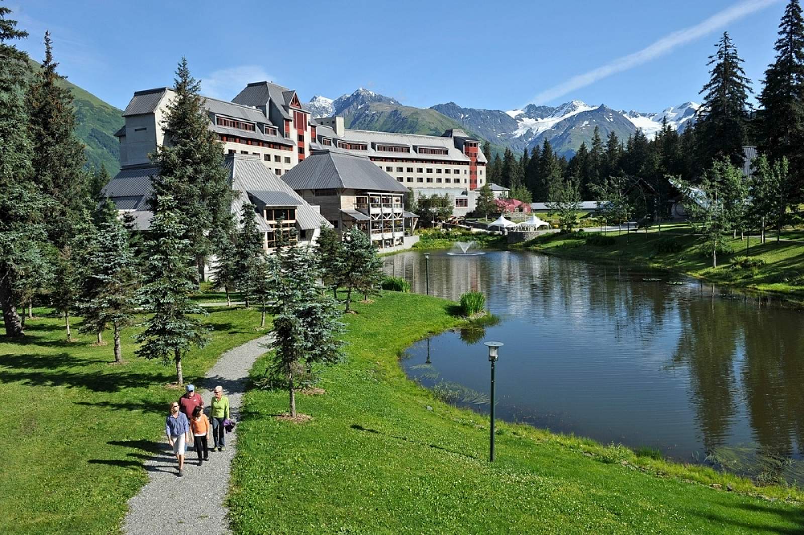Alyeska Resort – Girdwood in USA - a couple of people walking down a path by a lake.