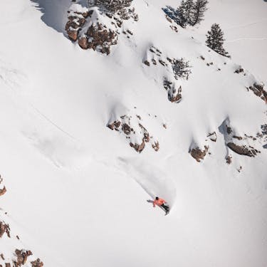 A skier skillfully making his way down the snowy slopes at Powder Mountain in Eden Utah. Snowboarders and snowmobiles are slightly visible in the winter sports-centric background.