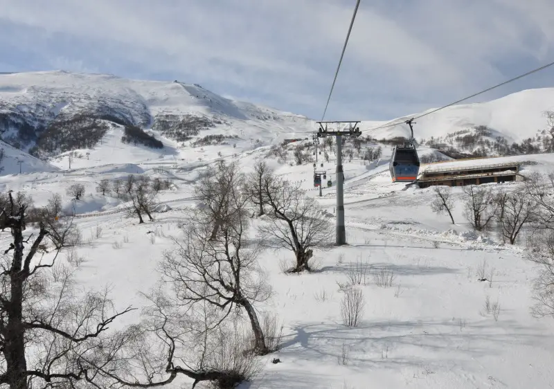Ski lift ascending a snowy mountain slope at Gudauri ski resort, Georgia. Chalet-style buildings dot the winter landscape draped in snow, reflecting an exhilarating winter sports ambiance.