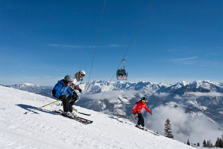 A lively winter sports scene at Feuerkogel – Ebensee in Upper Austria, featuring a ski lift transporting skiers to the top of the snow-covered resort. A chalet is visible in the background, and a skier is gracefully descending the slopes.
