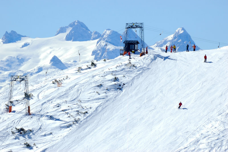Winter sports enthusiasts enjoy the day at the Feuerkogel – Ebensee ski resort in Salzkammergut, Austria, featuring a charming challet and efficient ski lift.