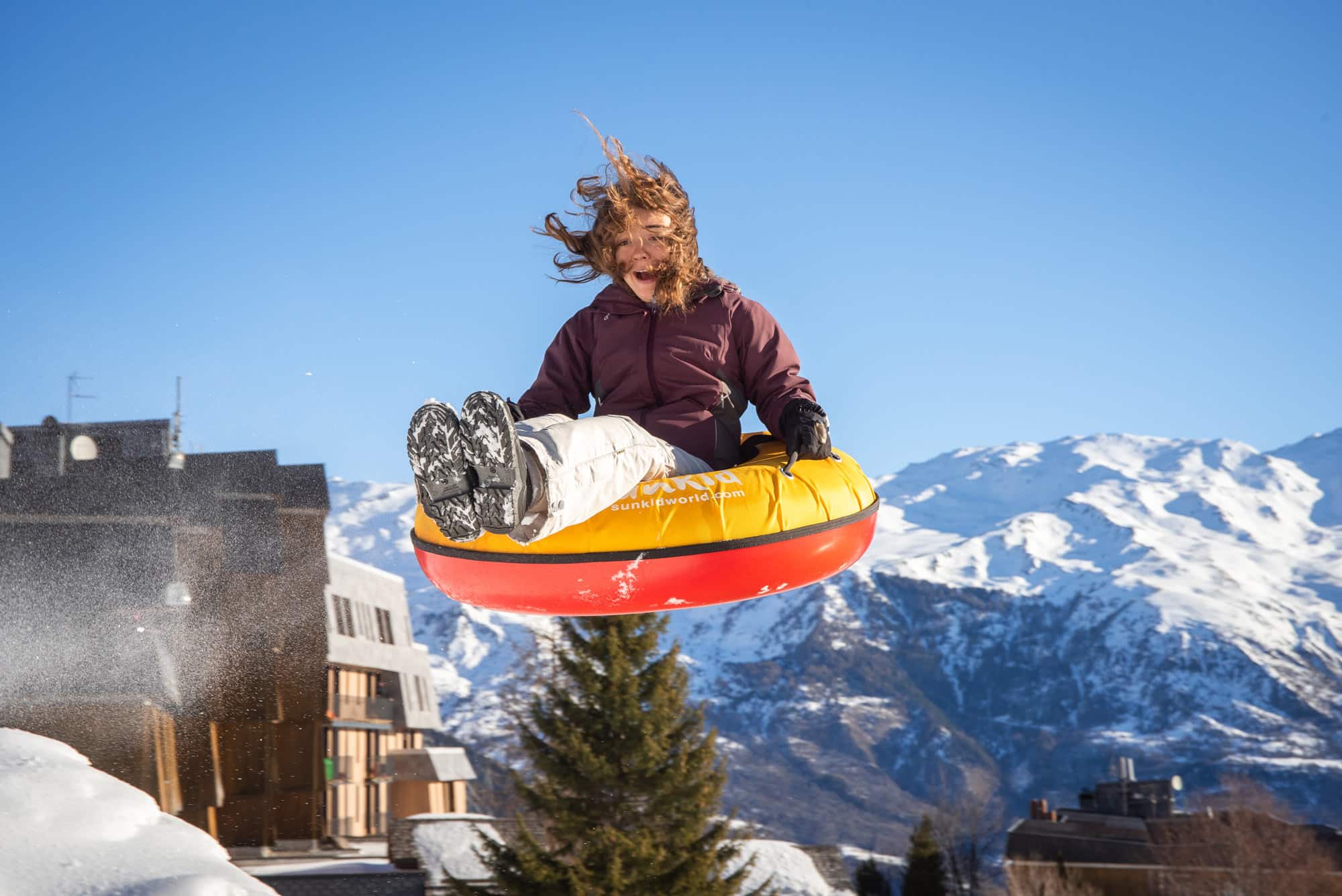 A thrilling winter sports scene in Karellis Savoie Mont Blanc France featuring a snowboarder and a skier gliding down the snow-covered slopes with a charming challet as a backdrop.