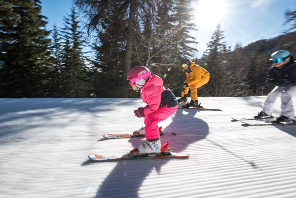 Family enjoying skiing at Karellis in Savoie Mont Blanc, France. A child is learning to ski on the snow-covered slopes of the beautiful ski resort.