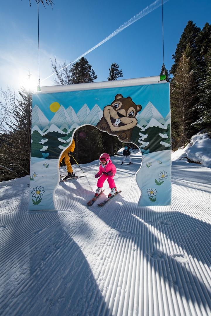 Winter scene in Karellis, Savoie Mont Blanc, Montricher-Albanne, France featuring bustling activity at a ski resort, with skiers and a snowboarder in motion, and a ski lift in the background.