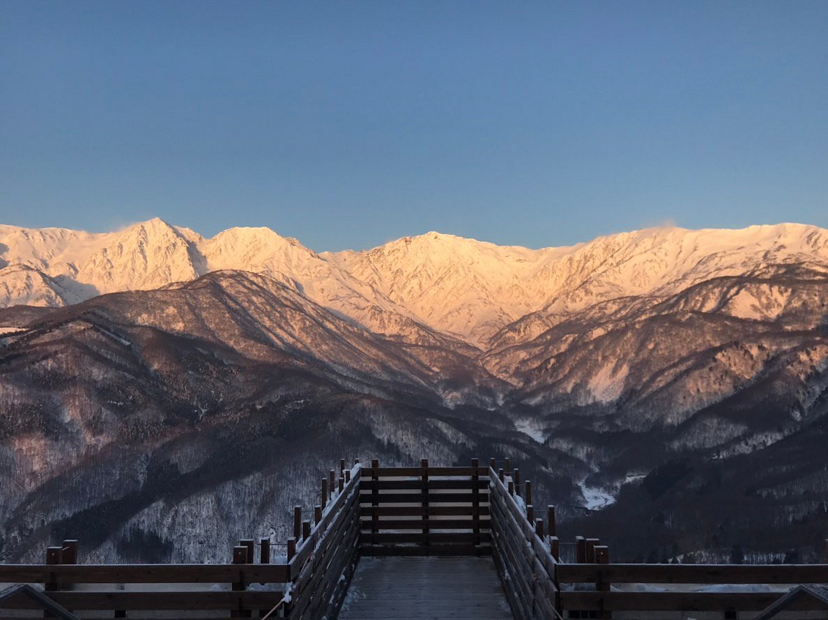 Hakuba Iwatake Mountain Resort in Japan - a wooden walkway leading to the top of a mountain with snow covered mountains in the background.