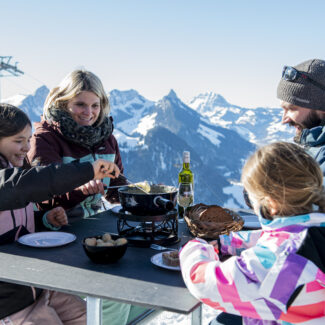 A snowy scene at Charmey ski resort Switzerland featuring a family enjoying winter sports. A chalet and a mountain hut dot the landscape.