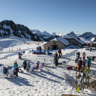 Winter sports scene at Charmey ski resort in Switzerland, featuring skiers enjoying the slopes and quaint chalet amidst the snowy landscape.