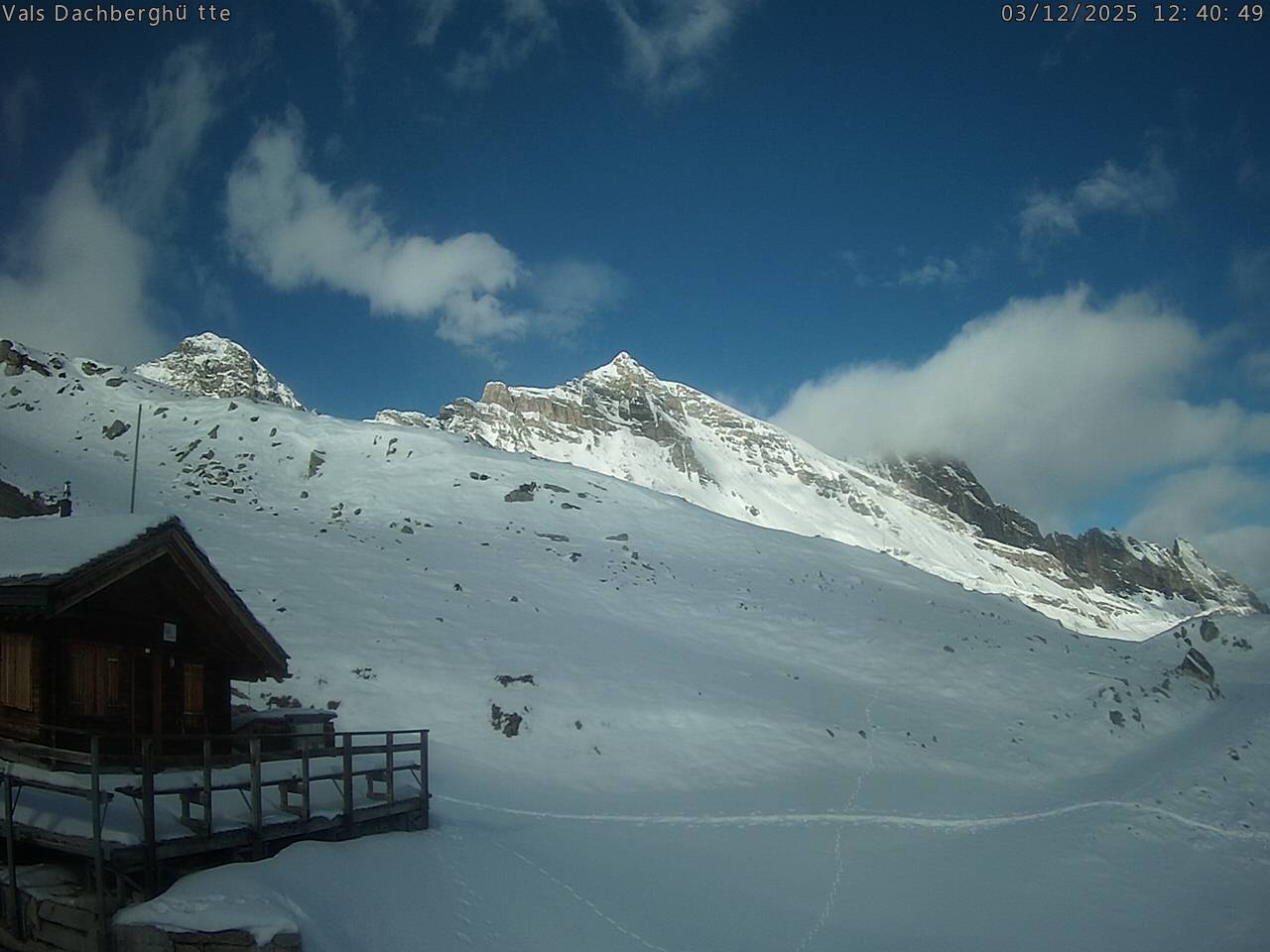 A serene view of Vals-Dachberg ski resort in eastern Switzerland featuring a mountain hut and chalet set against a picturesque mountain backdrop buzzing with winter sports activities.