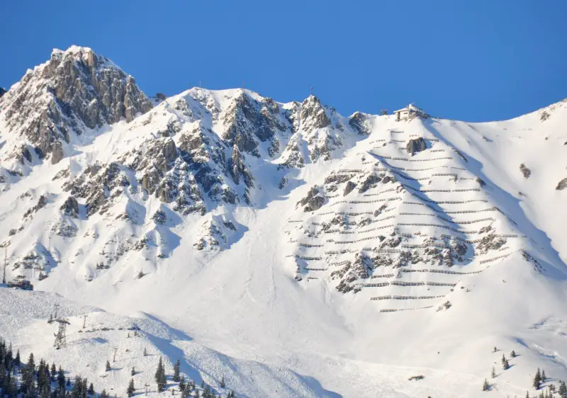 A snowy mountain scape at Nordkette – Innsbruck in the Tyrol region of Austria featuring a ski resort chalet a skier descending the slopes and snow-covered terrains.