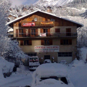 View of Le Seignus winter sports centre in Alpes-de-Haute-Provence, France; featuring a chalet, ski resort amenities, and a nearby mountain hut, all surrounded by snowy slopes.
