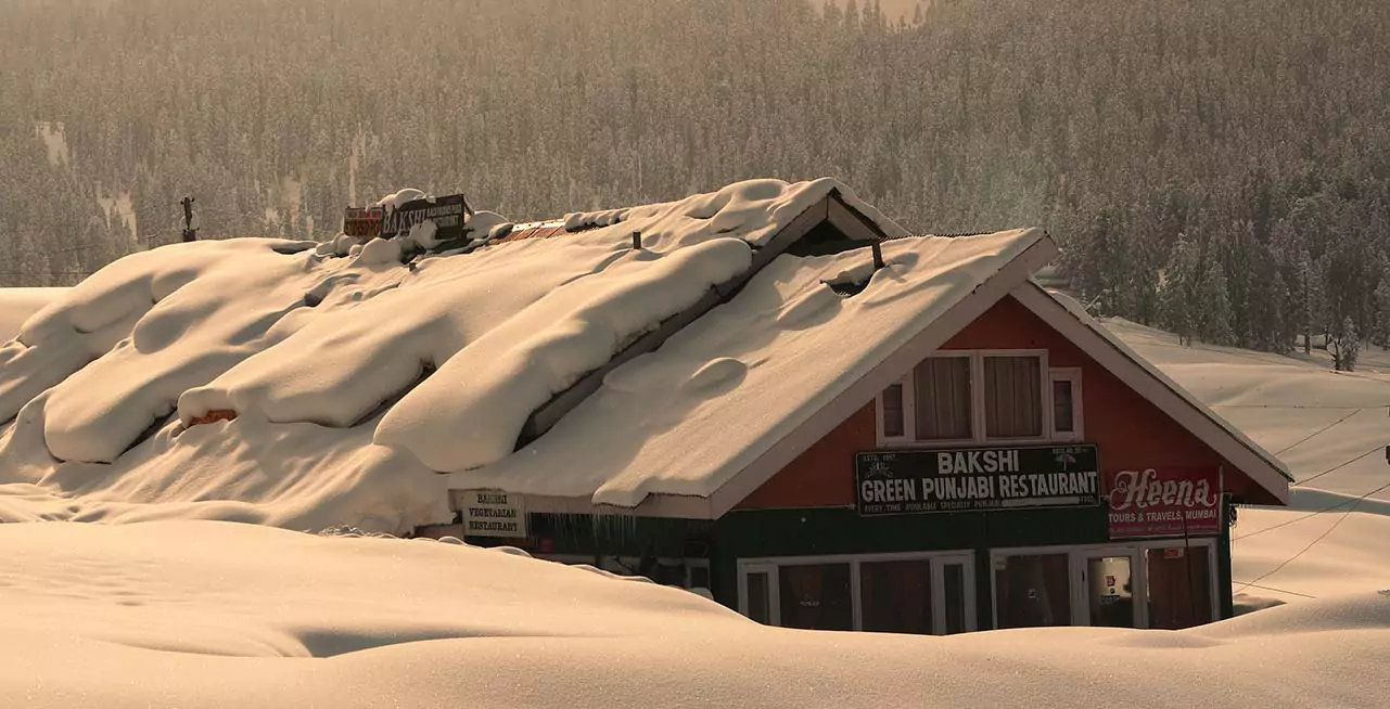 Gulmarg Ski Resort in India - a house covered in snow next to a forest.
